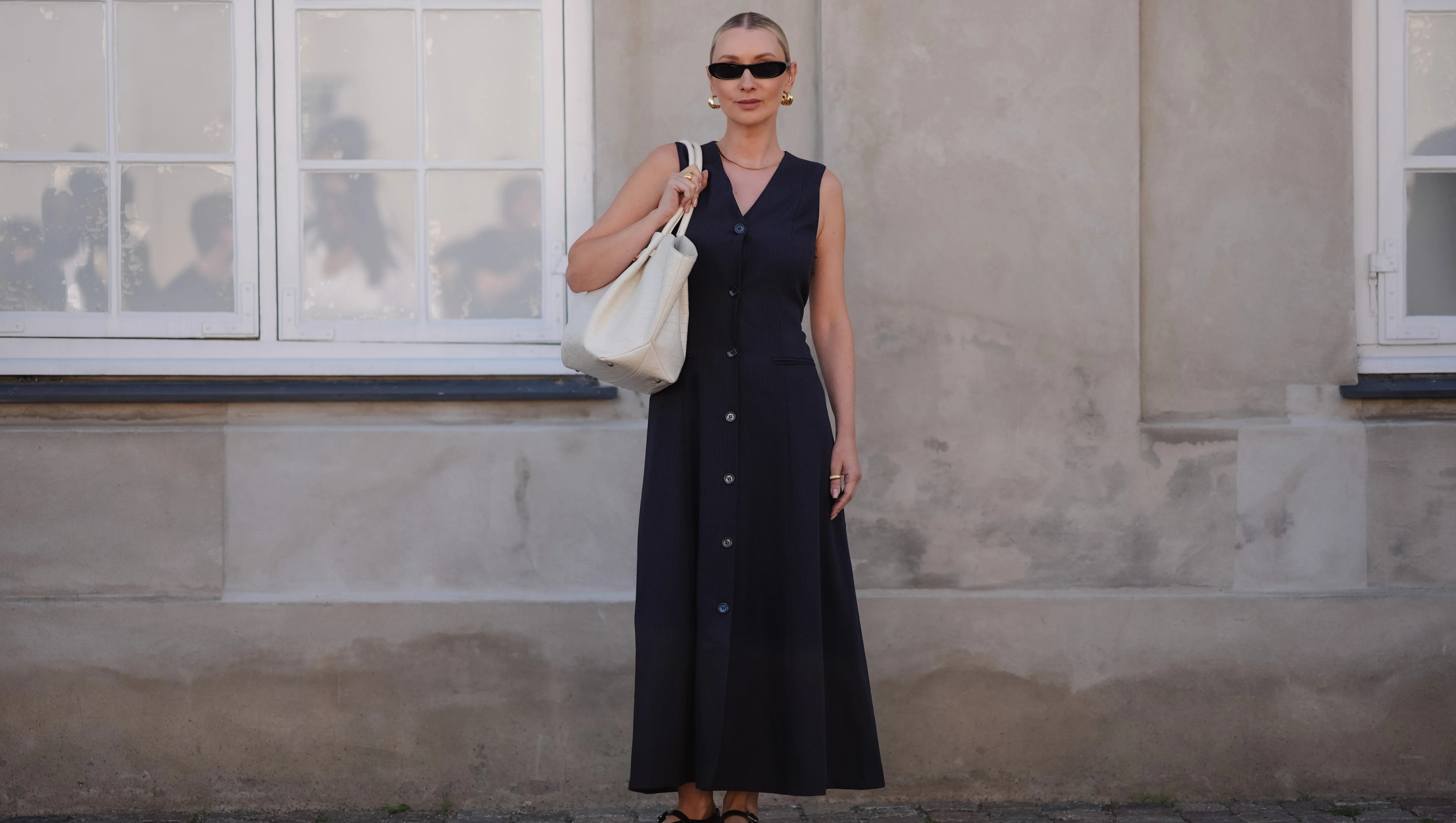 COPENHAGEN, DENMARK - AUGUST 6: Justyna Czerniak wears black sunglasses, gold earrings, black tailored vest midi dress, gold necklace, gold rings, cream DeMellier leather bag, black Alaia sheer mesh ballet flats, outside Lovechild 1979, during the Copenhagen Fashion Week Spring/Summer 2024-2025 on August 6, 2024 in Copenhagen, Denmark. (Photo by Edward Berthelot/Getty Images)