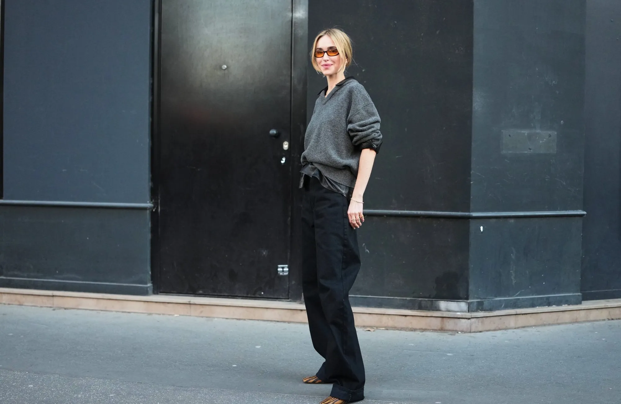 PARIS, FRANCE - MARCH 04: A guest wears blonde hair in a low bun, orange tinted sunglasses, a dark gray knit V neck wool sweater, a gold necklace, black wide leg balloon pants, a black leather with silver buckle belt, brown and black zebra print pattern leather pumps shoes, outside Acne Studios, during Paris Fashion Week - Womenswear Fall/Winter 2026/2027, on March 04, 2026 in Paris, France (Photo by Edward Berthelot/Getty Images)