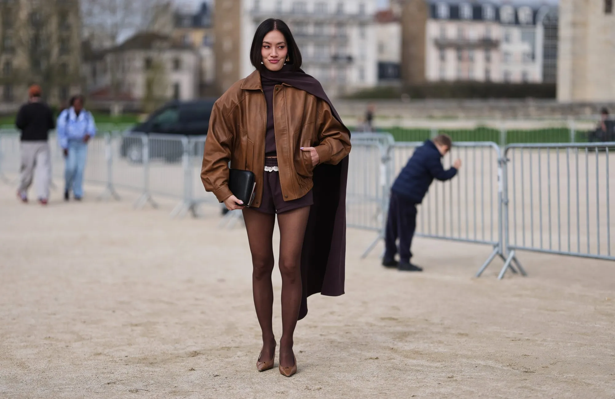 PARIS, FRANCE - MARCH 06: Tiffany Hsu wears black hair in a bob haircut, gold earrings, a brown leather oversized jacket, a dark brown knit turtleneck top with long scarf, dark brown fitted shorts, a black leather handbag, brown tights, dark brown leather pointed pumps shoes, outside Loewe, during Paris Fashion Week - Womenswear Fall/Winter 2026/2027, on March 06, 2026 in Paris, France (Photo by Edward Berthelot/Getty Images)