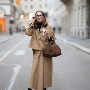 MILAN, ITALY - FEBRUARY 28: Annette Weber is seen wearing a camel colored button up overshirt with a relaxed silhouette and oversized flap chest pockets from Max Mara; a black fitted turtleneck from Max Mara; a matching camel colored midi skirt with a fluid fabric straight cut from Max Mara; a structured brown suede nubuk leather bag with top handles, a soft rounded shape and zip closure from Max Mara; sculptural oversized gold tone earrings with rounded elements from Max Mara; oversized eyeglasses with a tortoiseshell pattern frame from Mango; among her jewelry are chunky gold rings with diamond detailing; holding a coffee to go cup; her shoulder length brown hair is worn straight with a center part during the Milan Fashion Week - Womenswear Fall/Winter 2026/2027 on February 28, 2026 in Milan, Italy. (Photo by Moritz Scholz/Getty Images)