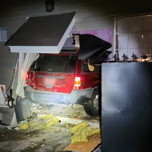 A photo shows a red SUV inside a mangled home