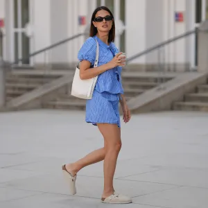 MUNICH, GERMANY - JUNE 15: Anna Winter is seen wearing a blue white striped shorts with drawstring detail from Rita Montezuma x NA-KD; a matching blue white striped blouse with tie and bow details in the front and puff sleeves from Rita Montezuma x NA-KD; a pair of off-white suede Boston slippers with rounded shape and open back from Birkenstock; a light cream white small Romy hobo leather bag with a slim shoulder strap and silver button logo detail from Tory Burch; a cream white reusable to go coffee cup with structural details from Huskee; a yellow golden B.zero 1 necklace with characteristic round pendant from Bvlgari; black rectangular Teru sunglasses from Ray-Ban; a golden Juste un Clou ring from Cartier; a golden Love ring from Cartier on June 15, 2025 in Munich, Germany. (Photo by Moritz Scholz/Getty Images)