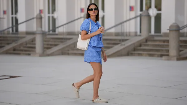 MUNICH, GERMANY - JUNE 15: Anna Winter is seen wearing a blue white striped shorts with drawstring detail from Rita Montezuma x NA-KD; a matching blue white striped blouse with tie and bow details in the front and puff sleeves from Rita Montezuma x NA-KD; a pair of off-white suede Boston slippers with rounded shape and open back from Birkenstock; a light cream white small Romy hobo leather bag with a slim shoulder strap and silver button logo detail from Tory Burch; a cream white reusable to go coffee cup with structural details from Huskee; a yellow golden B.zero 1 necklace with characteristic round pendant from Bvlgari; black rectangular Teru sunglasses from Ray-Ban; a golden Juste un Clou ring from Cartier; a golden Love ring from Cartier on June 15, 2025 in Munich, Germany. (Photo by Moritz Scholz/Getty Images)