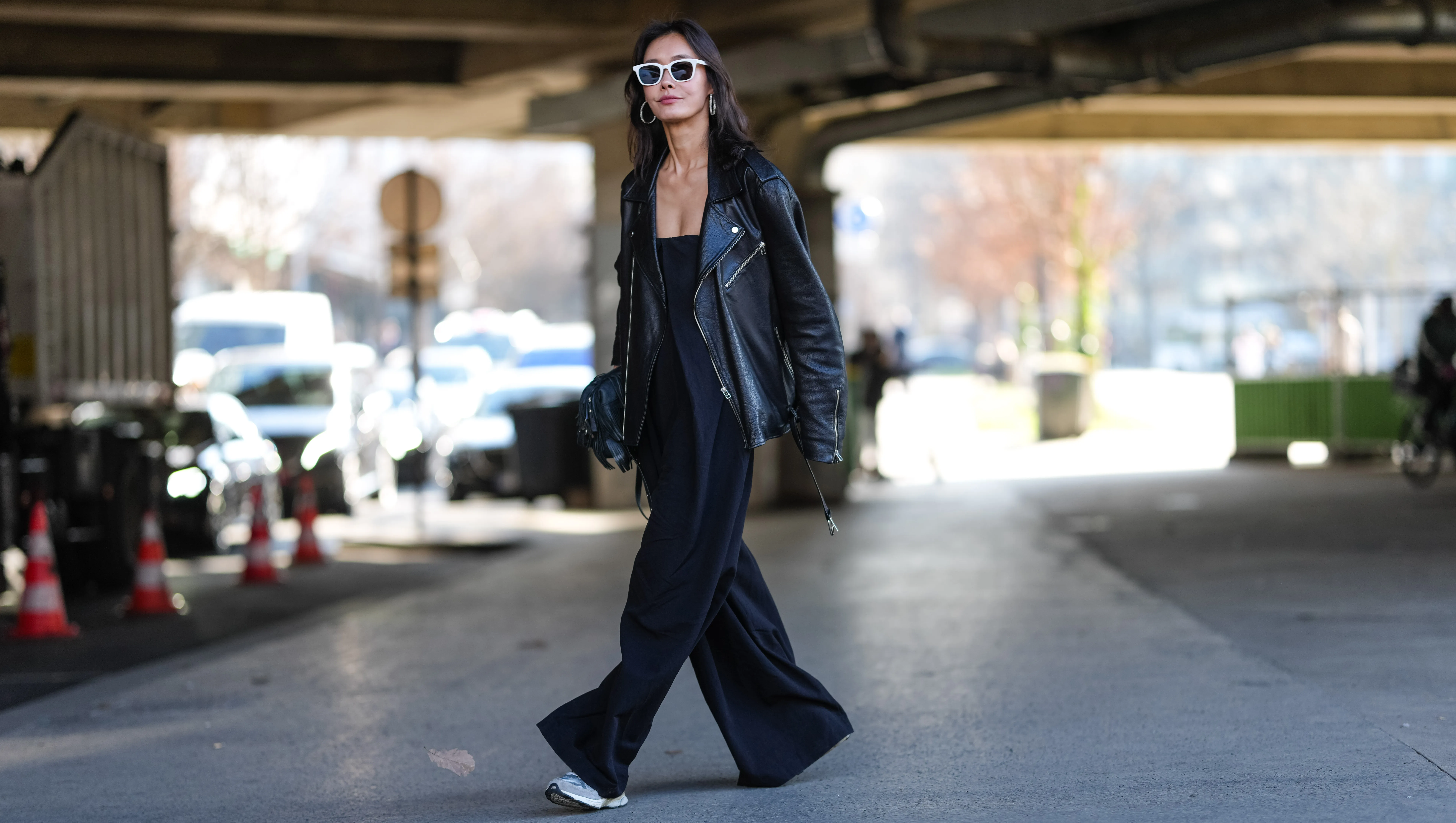 PARIS, FRANCE - MARCH 05: A guest wears white sunglasses, silver hoop earrings, shiny black oversized leather jacket, shiny black leather bag, black sleeveless flowy romper, light gray sneaker shoes, outside Stella McCartney, during the Paris Fashion week Women's Fall/Winter 2025-2026 on March 5, 2025 in Paris, France. (Photo by Edward Berthelot/Getty Images)