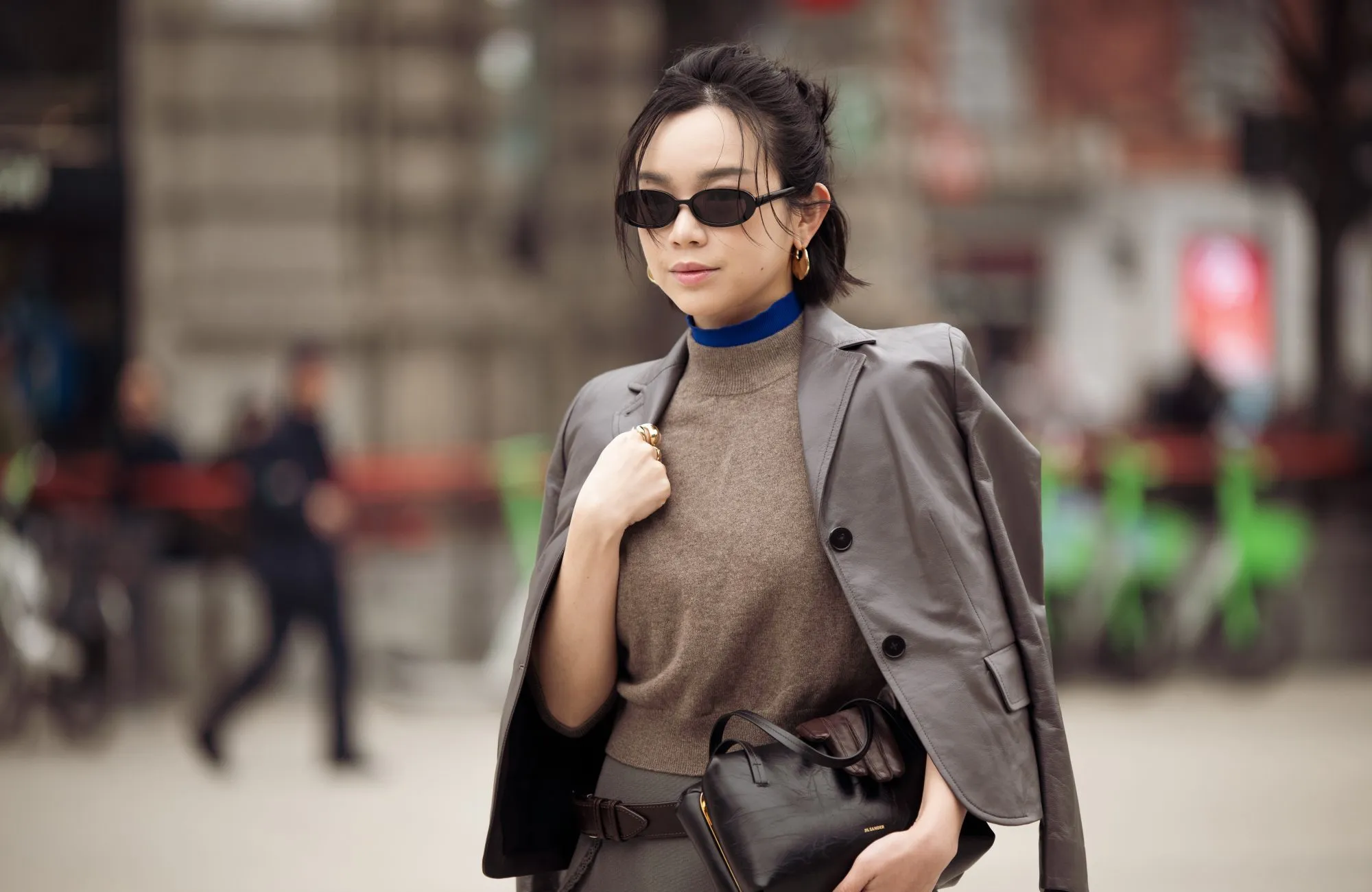 MILAN, ITALY - FEBRUARY 25: Willabelle Ong wears a cropped grey tailored blazer in smooth suiting fabric draped over the shoulders, layered over a taupe sleeveless knit top with a bright cobalt blue high-neck under layer, paired with a grey mini skirt in wool blend, accessorised with slim black rectangular sunglasses, gold hoop earrings and a wide brown leather belt with silver buckle, carrying a black leather clutch outside Jil Sander during the Milan Fashion Week - Womenswear Fall/Winter 2026/2027 on February 25, 2026 in Milan, Italy. (Photo by Raimonda Kulikauskiene/Getty Images)