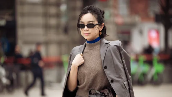 MILAN, ITALY - FEBRUARY 25: Willabelle Ong wears a cropped grey tailored blazer in smooth suiting fabric draped over the shoulders, layered over a taupe sleeveless knit top with a bright cobalt blue high-neck under layer, paired with a grey mini skirt in wool blend, accessorised with slim black rectangular sunglasses, gold hoop earrings and a wide brown leather belt with silver buckle, carrying a black leather clutch outside Jil Sander during the Milan Fashion Week - Womenswear Fall/Winter 2026/2027 on February 25, 2026 in Milan, Italy. (Photo by Raimonda Kulikauskiene/Getty Images)