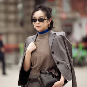 MILAN, ITALY - FEBRUARY 25: Willabelle Ong wears a cropped grey tailored blazer in smooth suiting fabric draped over the shoulders, layered over a taupe sleeveless knit top with a bright cobalt blue high-neck under layer, paired with a grey mini skirt in wool blend, accessorised with slim black rectangular sunglasses, gold hoop earrings and a wide brown leather belt with silver buckle, carrying a black leather clutch outside Jil Sander during the Milan Fashion Week - Womenswear Fall/Winter 2026/2027 on February 25, 2026 in Milan, Italy. (Photo by Raimonda Kulikauskiene/Getty Images)