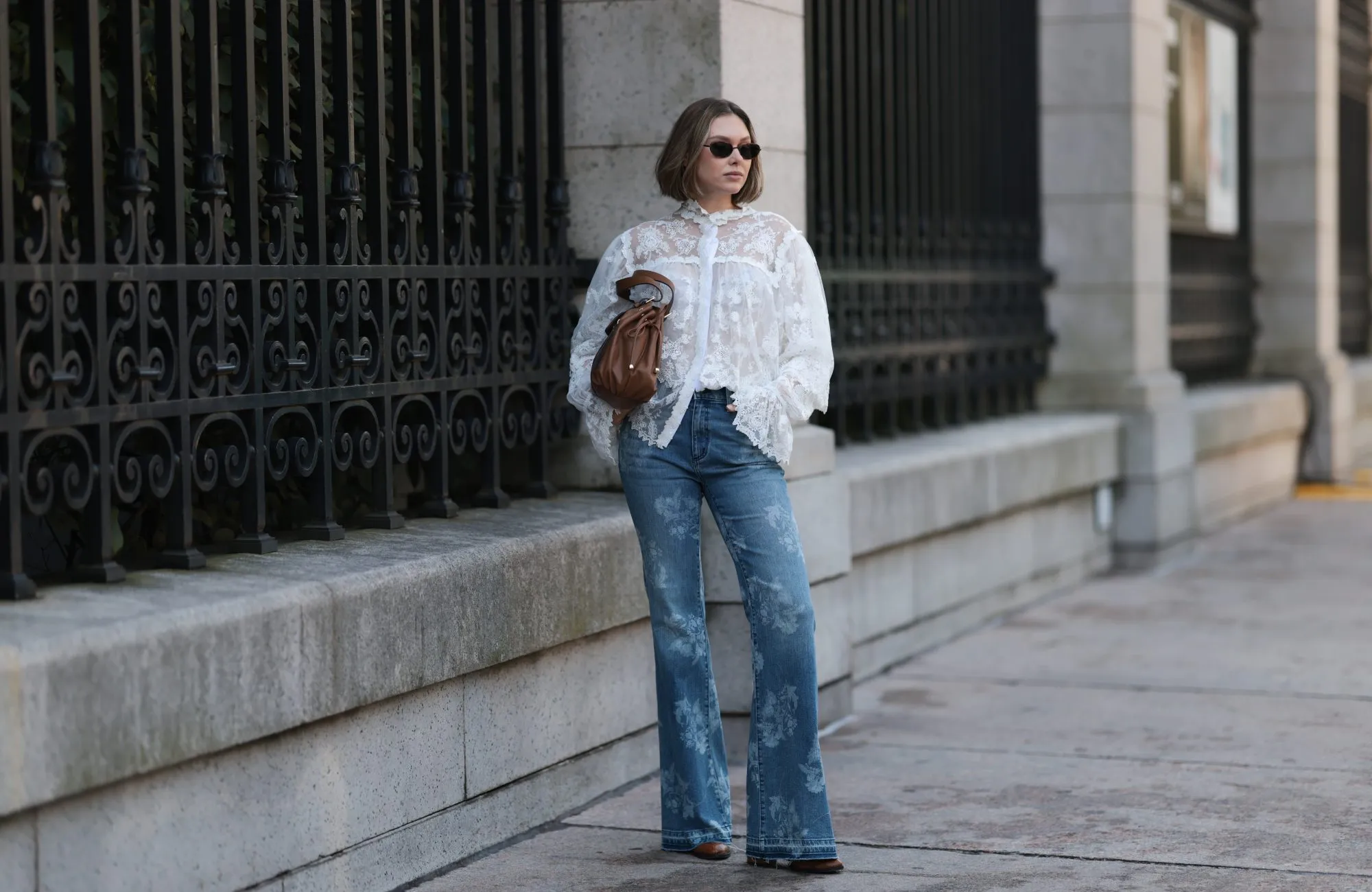 NEW YORK, NEW YORK - SEPTEMBER 14: Kate Smolianinova seen wearing Vehla Eyewear slim rectangular sunglasses in a dark brown. Her hair styled in a sleek chin-length bob with a soft middle part. A Kobi Halperin sheer white lace blouse with floral embroidery, high ruffled collar, voluminous sleeves and scalloped edges, paired with Kobi Halperin blue high-waist flared jeans featuring tonal floral jacquard detailing, a Gerard Darel soft brown leather handbag with gathered pleats and rounded handles and Dear Frances brown pointed-toe leather boots, peeking under the flared hem, outside the Ulla Johnson show, during New York Fashion Week, on September 14, 2025 in New York City. (Photo by Jeremy Moeller/Getty Images)