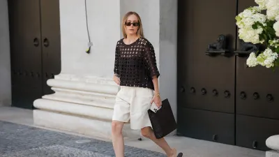 MUNICH, GERMANY - JULY 1: Anouk Delphine is seen wearing an H&M dark brown crochet t-shirt with three-quarter sleeves; a pair of beige Cos bermuda pants; a black squared weaved Cos hand bag; her blond hair is worn straight; black leather low heeled H&M thong sandals; a pair of oval Gucci sunglasses; a vintage gold Seiko watch; a Cartier light point gold necklace; Cartier bracelets; a gold Cartier brilliant-cut diamond ring paved with brilliant-cut diamonds; a Juste un Clou Cartier golden ring; she holds an iPhone in her hand on July 1, 2025 in Munich, Germany. (Photo by Moritz Scholz/Getty Images)