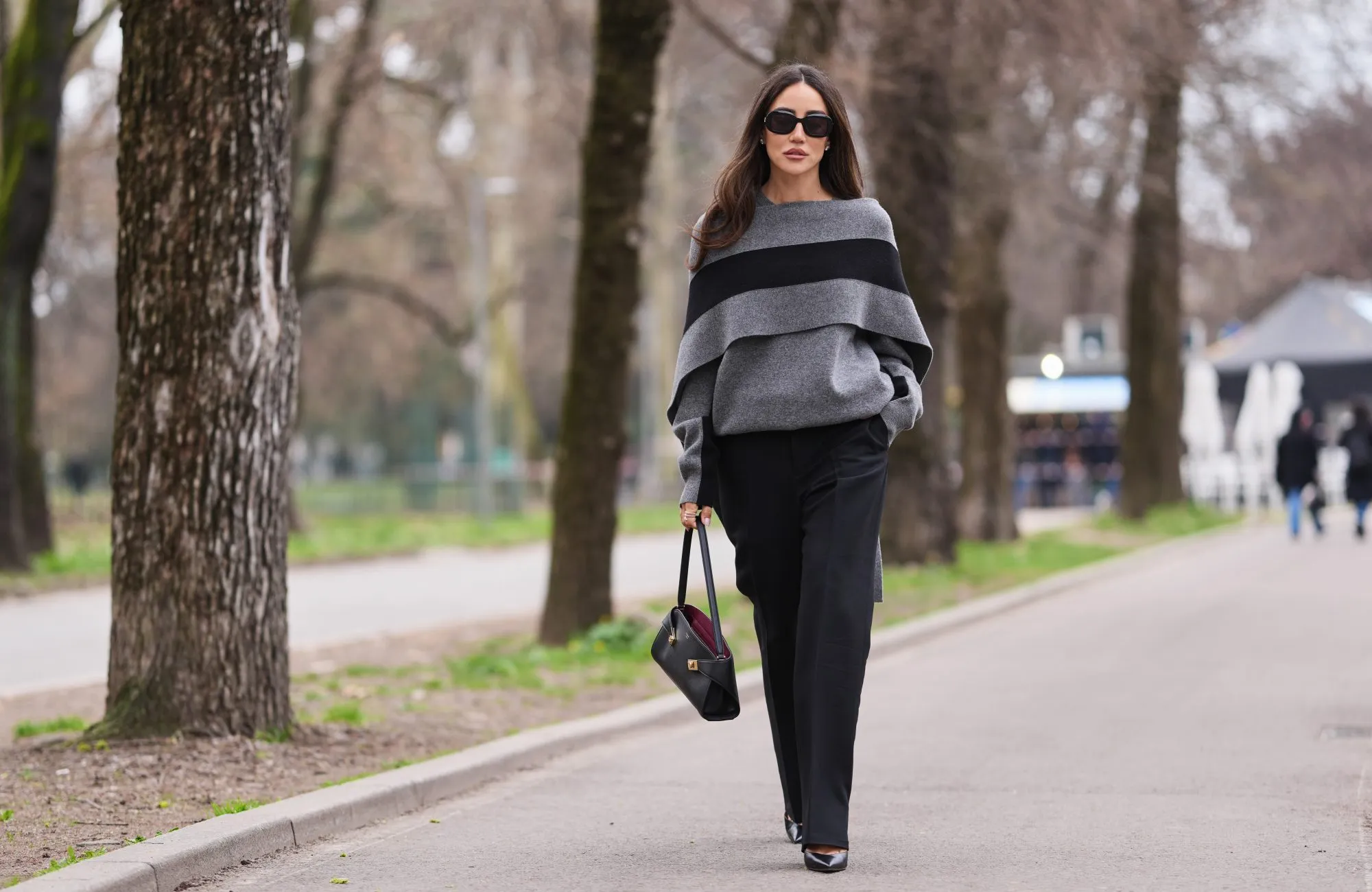 MILAN, ITALY - FEBRUARY 28: Tamara Kalinic wears brown long hair, black sunglasses, a gray knit poncho sweater with a large black stripe, black wide leg trousers, a black leather bag, black leather pumps shoes, outside Ferragamo, during Milan Fashion Week - Womenswear Fall/Winter 2026/2027, on February 28, 2026 in Milan, Italy (Photo by Edward Berthelot/Getty Images)