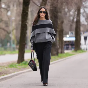 MILAN, ITALY - FEBRUARY 28: Tamara Kalinic wears brown long hair, black sunglasses, a gray knit poncho sweater with a large black stripe, black wide leg trousers, a black leather bag, black leather pumps shoes, outside Ferragamo, during Milan Fashion Week - Womenswear Fall/Winter 2026/2027, on February 28, 2026 in Milan, Italy (Photo by Edward Berthelot/Getty Images)