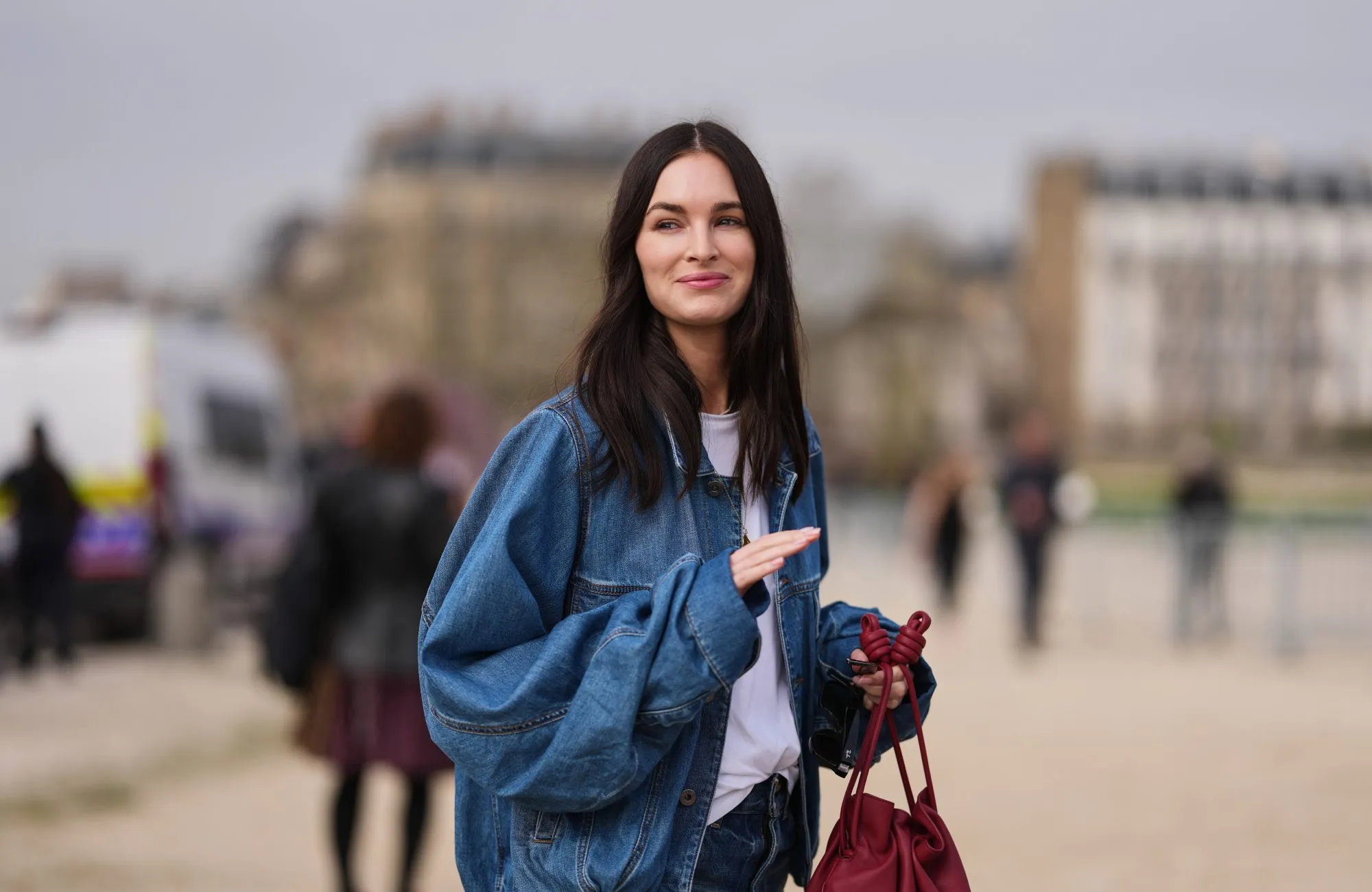 PARIS, FRANCE - MARCH 06: A guest wears dark brown hair, a blue denim jacket, a white cotton T-shirt, blue denim bootcut jeans, a red leather handbag, outside Loewe, during Paris Fashion Week - Womenswear Fall/Winter 2026/2027, on March 06, 2026 in Paris, France (Photo by Edward Berthelot/Getty Images)