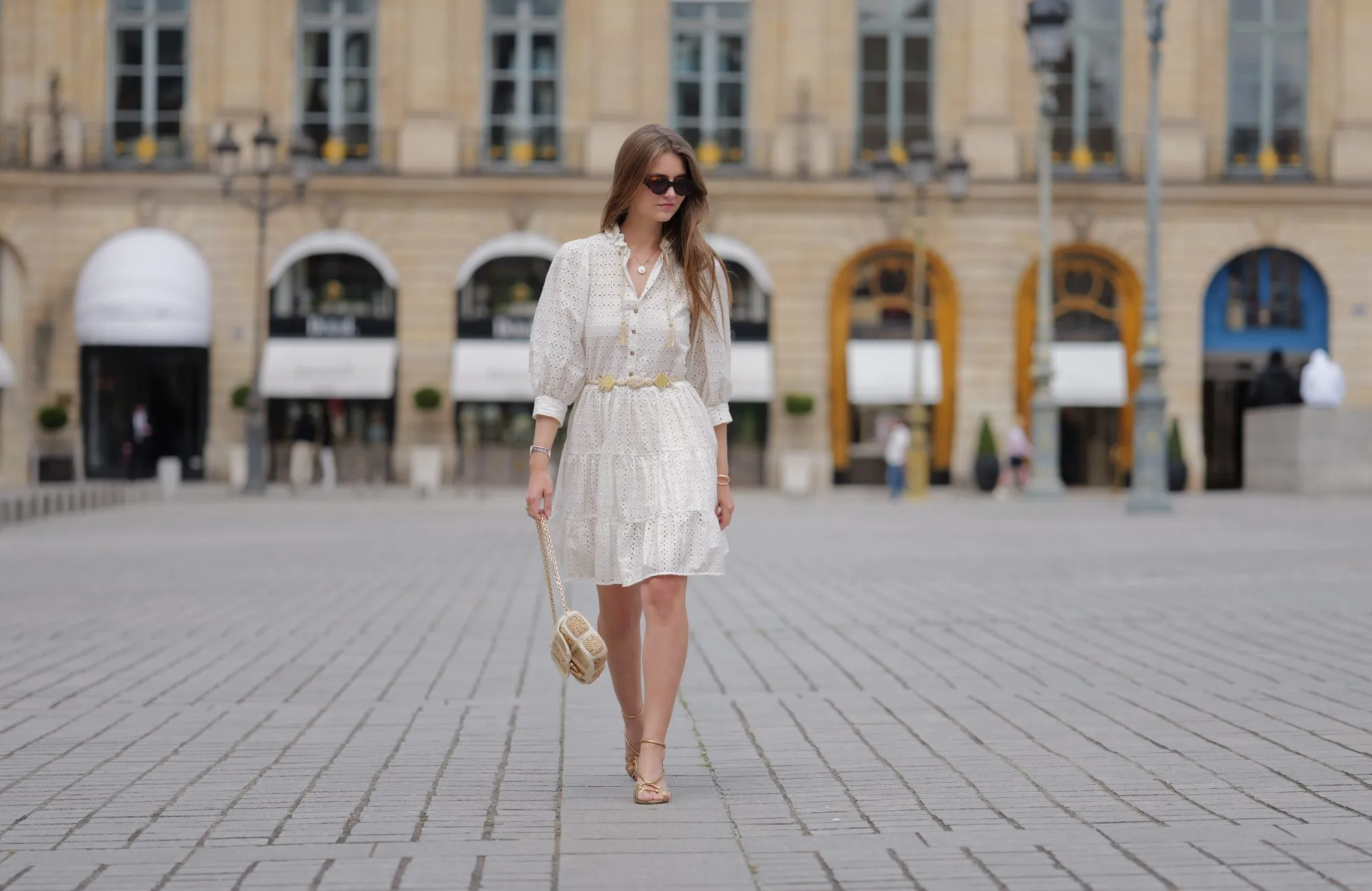 PARIS, FRANCE - JUNE 14: Segolene Hyppolite wears sunglasses, a white mini pleated and gathered summer dress with floral embroidery and long sleeves from Anne Fontaine, a rope belt from Anne Fontaine, a raffia bag from Vanessa Bruno, golden sandals / shoes from Sezane, during a street style fashion photo session, on June 14, 2024 in Paris, France. (Photo by Edward Berthelot/Getty Images)