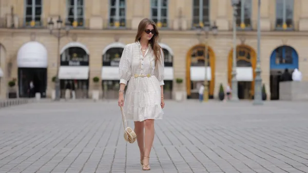 PARIS, FRANCE - JUNE 14: Segolene Hyppolite wears sunglasses, a white mini pleated and gathered summer dress with floral embroidery and long sleeves from Anne Fontaine, a rope belt from Anne Fontaine, a raffia bag from Vanessa Bruno, golden sandals / shoes from Sezane, during a street style fashion photo session, on June 14, 2024 in Paris, France. (Photo by Edward Berthelot/Getty Images)