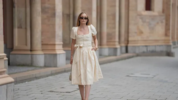 MUNICH, GERMANY - SEPTEMBER 12: Anouk Delphine is seen wearing a cream-colored midi dress with subtle floral jacquard, puff sleeves, a square neckleine and a waist bow from Limberry; open-toe heeled sandals in a soft ivory shade, detailed with oversized floral appliqués from Zara; a small structured handbag in the shape of a heart covered in shimmering metallic texture from Weat; a golden watch with a metallic wristband from Vintage Seiko; narrow dark sunglasses with brown tinted lenses from Gucci; her blonde hair is worn loose on September 12, 2025 in Munich, Germany. (Photo by Moritz Scholz/Getty Images)