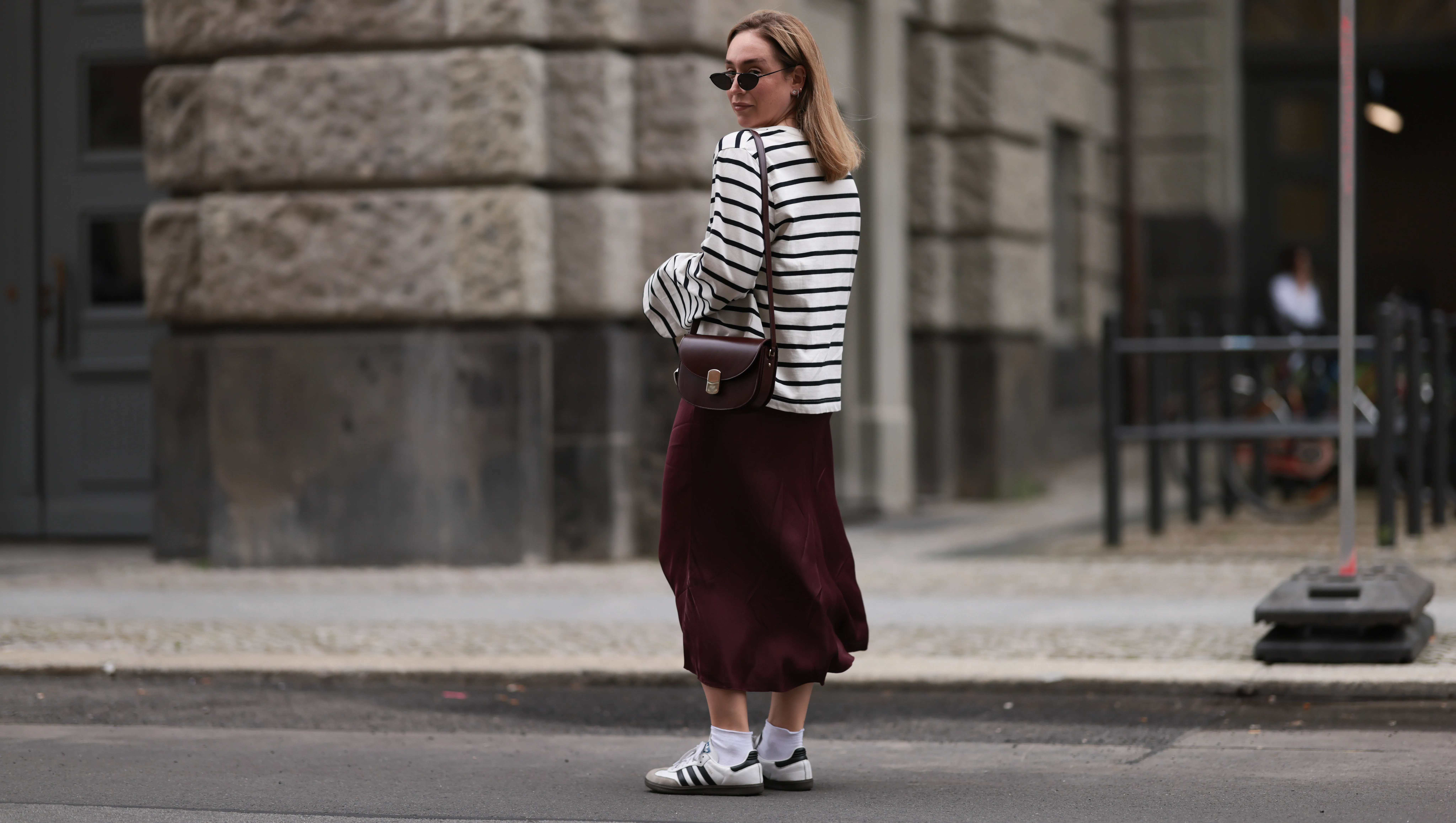 BERLIN, GERMANY - JULY 13: Sonia Lyson is seen wearing several silver and golden earrings and ear studs; a black, oval sunglasses with filigree metal frame from Yves Saint Laurent; a white sweatshirt with black stripes and loose fit from Zara; a burgundy satin midi skirt from Zara; a burgundy leather bag from S&eacute;zane; white socks and white Samba sneakers from Adidas on July 13, 2024 in Berlin, Germany. (Photo by Jeremy Moeller/Getty Images)