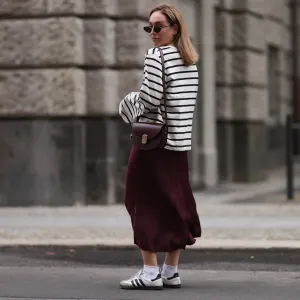 BERLIN, GERMANY - JULY 13: Sonia Lyson is seen wearing several silver and golden earrings and ear studs; a black, oval sunglasses with filigree metal frame from Yves Saint Laurent; a white sweatshirt with black stripes and loose fit from Zara; a burgundy satin midi skirt from Zara; a burgundy leather bag from Sézane; white socks and white Samba sneakers from Adidas on July 13, 2024 in Berlin, Germany. (Photo by Jeremy Moeller/Getty Images)