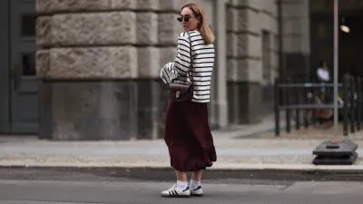 BERLIN, GERMANY - JULY 13: Sonia Lyson is seen wearing several silver and golden earrings and ear studs; a black, oval sunglasses with filigree metal frame from Yves Saint Laurent; a white sweatshirt with black stripes and loose fit from Zara; a burgundy satin midi skirt from Zara; a burgundy leather bag from Sézane; white socks and white Samba sneakers from Adidas on July 13, 2024 in Berlin, Germany. (Photo by Jeremy Moeller/Getty Images)
