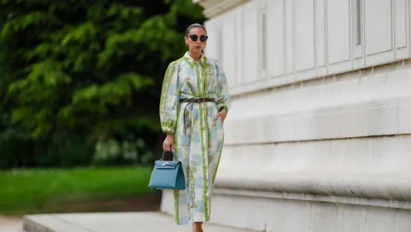 PARIS, FRANCE - MAY 12: Gabriella Berdugo wears sunglasses, earrings, a white blue and green checked long dress with long sleeves and floral print, a brown leather belt, a blue Kelly Hermes bag, pale pastel yellow mules / shoes with heart-shaped heels from Kat Maconie, during a street style fashion photo session, on May 12, 2024 in Paris, France. (Photo by Edward Berthelot/Getty Images)