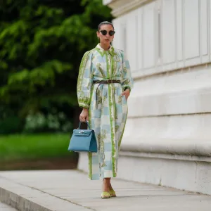 PARIS, FRANCE - MAY 12: Gabriella Berdugo wears sunglasses, earrings, a white blue and green checked long dress with long sleeves and floral print, a brown leather belt, a blue Kelly Hermes bag, pale pastel yellow mules / shoes with heart-shaped heels from Kat Maconie, during a street style fashion photo session, on May 12, 2024 in Paris, France. (Photo by Edward Berthelot/Getty Images)