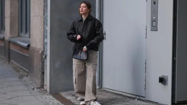BERLIN, GERMANY - FEBRUARY 19: Sophia Geiss seen wearing a black woven leather jacket by Second Female layered over a minimalist H&M Studio look featuring a light beige high-neck top and oversized cargo trousers in a matching neutral tone. She pairs the outfit with Miu Miu x New Balance sneakers in white with brown detailing. Accessories include a structured black YSL black shoulder bag with gold hardware, Mango sunglasses held in her hand, and subtle silver hoop earrings. Her hair is styled in a loose low updo on February 19, 2026 in Berlin, Germany. (Photo by Jeremy Moeller/Getty Images)