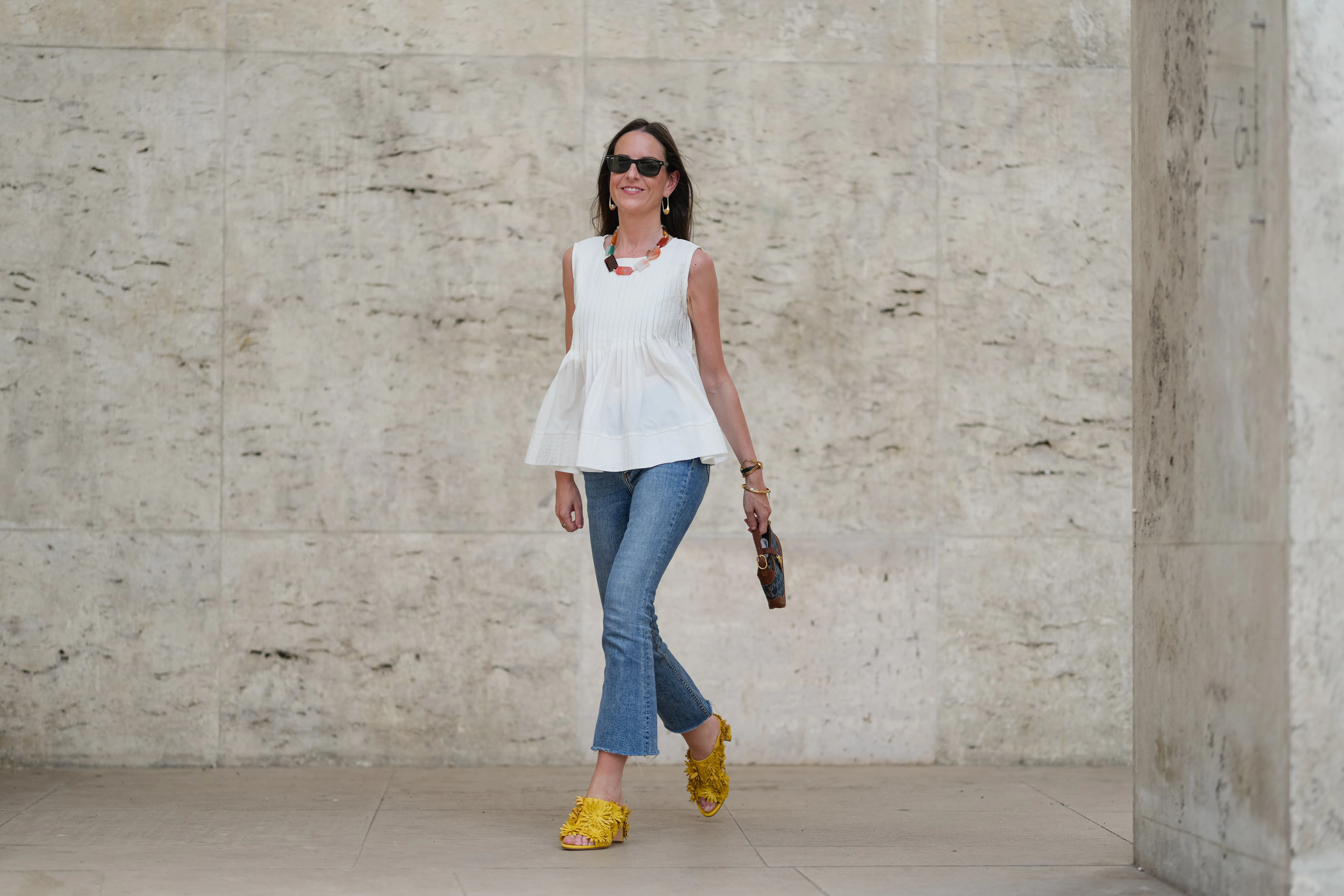 PARIS, FRANCE - MAY 02: Alba Garavito Torre wears black sunglasses, long straight brown hair with a center part, a white pleated peplum sleeveless blouse by Commense, and blue high-rise raw-hem denim jeans. A yellow clog sandal with floral detailing by AGL is worn, paired with a jean denim and brown mini Jackie handbag by Gucci. Accessories include a chunky necklace with colorful natural stones by Sempiterno Paris and gold jewelry. Full body shot, during a street style fashion photo session, on May 02, 2025 in Paris, France. (Photo by Edward Berthelot/Getty Images)
