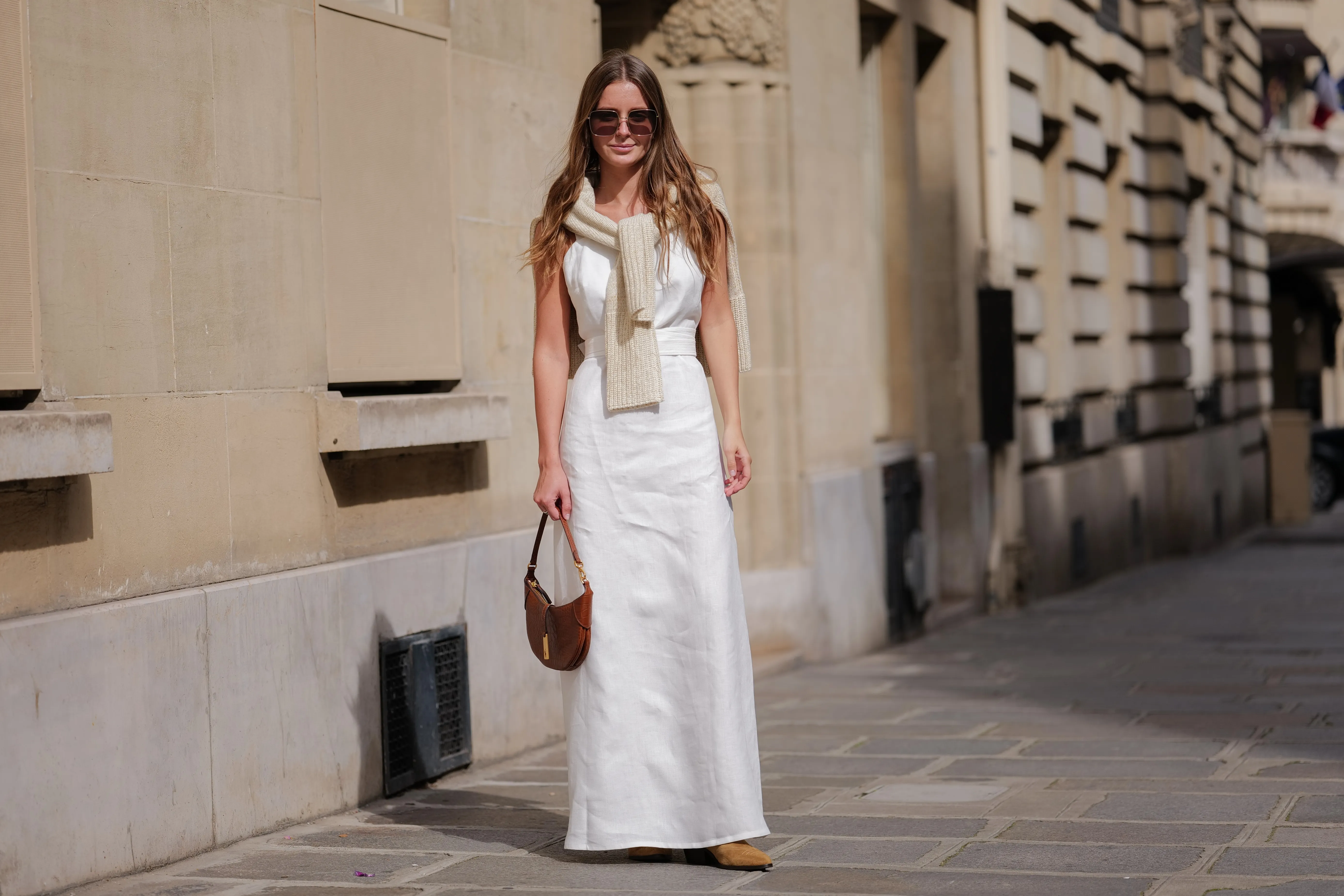 PARIS, FRANCE - APRIL 28: Diane Batoukina wears dark brown large squared sunglasses from Dior, a white square-neck / linen belted long dress, a white latte ribbed wool pullover knot at the shoulder, a camel brown shiny leather crocodile print pattern handbag from Ralph Lauren, brown suede block heels / pointed ankle boots , during a street style fashion photo session, on April 28, 2023 in Paris, France. (Photo by Edward Berthelot/Getty Images)