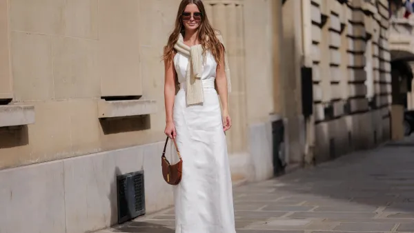 PARIS, FRANCE - APRIL 28: Diane Batoukina wears dark brown large squared sunglasses from Dior, a white square-neck / linen belted long dress, a white latte ribbed wool pullover knot at the shoulder, a camel brown shiny leather crocodile print pattern handbag from Ralph Lauren, brown suede block heels / pointed ankle boots , during a street style fashion photo session, on April 28, 2023 in Paris, France. (Photo by Edward Berthelot/Getty Images)