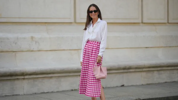 Alba Garavito Torre wears black sunglasses from Ray Ban, white pearl and gold chain pendant earrings, a transparent large pearls long necklace, a white shirt, pink and white checkered print pattern midi pants from Frambuã, gold bracelets, a pale pink matte leather handbag from Saonara Brand, white latte matte shiny leather block heels mules from Jonak, during a street style fashion photo session, on June 06, 2023 in Paris, France.