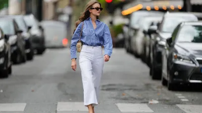 Segolene Hyppolite wears sunglasses, a blue and white oversized shirt from Tommy Hilfiger, a raffia beige bag from Vanessa Bruno, high waist white denim pants from Vanessa Bruno, Chanel slingback shoes in blue denim with black tips, during a street style fashion photo session, on May 20, 2024 in Paris, France.