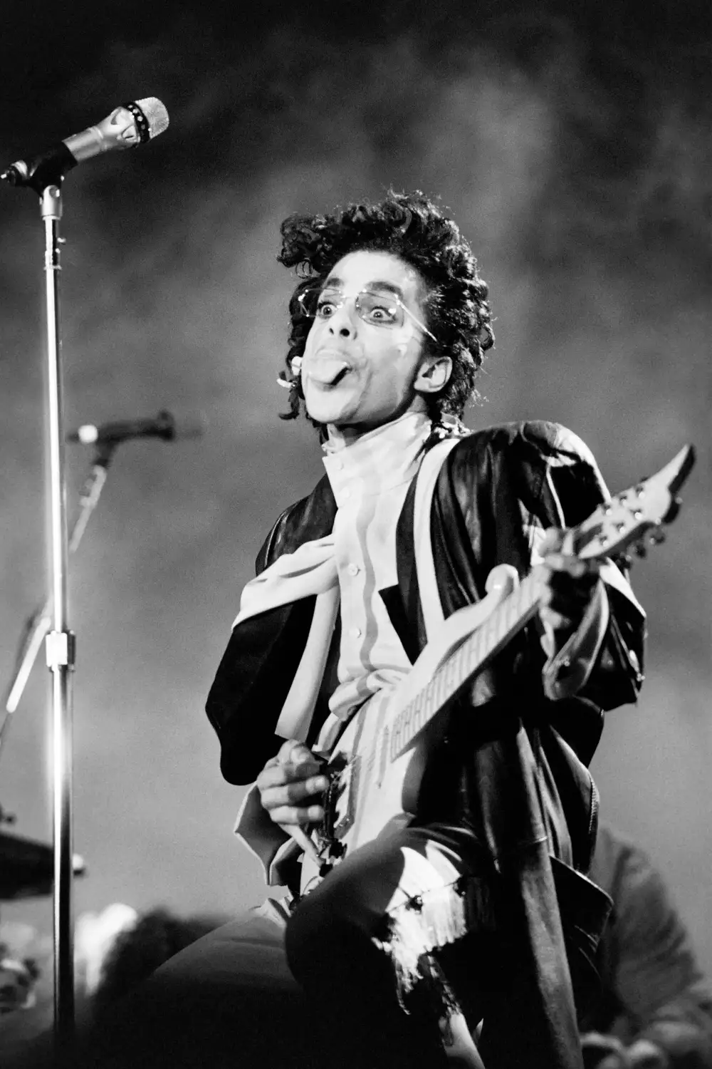 Prince sticking out his tongue on stage while playing guitar.