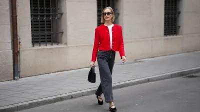 MUNICH, GERMANY - MARCH 27: Marlies Pia Pfeifhofer is seen wearing a red knit "Janker" cardigan featuring decorative silver buttons from La Foresta; a white cotton short sleeve T-shirt with padded shoulders from The Attico; dark grey cropped denim jeans with a straight leg from Sézane; black velvet pointed toe ballet flats with a crossover Mary Jane strap and gold tone charm hardware detailing from La Foresta x Flabelus; a black leather "Gunther" mini bag with a compact structured silhouette and a tonal circular passementerie disc detail from Destree; small black acetate cat eye sunglasses with dark lenses called "Blum" from Kaleos; delicate gold "Eva" hoop earrings from Sézane; her blonde hair is styled in a straight chin length bob with a center part on March 27, 2026 in Munich, Germany. (Photo by Moritz Scholz/Getty Images)