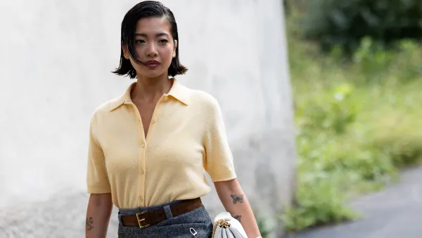 MILAN, ITALY - SEPTEMBER 25: A guest wears a polo styled light yellow short sleeved cardigan, a brown leather belt, a white leather bag and a grey mini skirt outside Prada show during the Milan Fashion Week Womenswear Spring/Summer 2026 on September 25, 2025 in Milan, Italy. (Photo by Valentina Frugiuele/Getty Images)