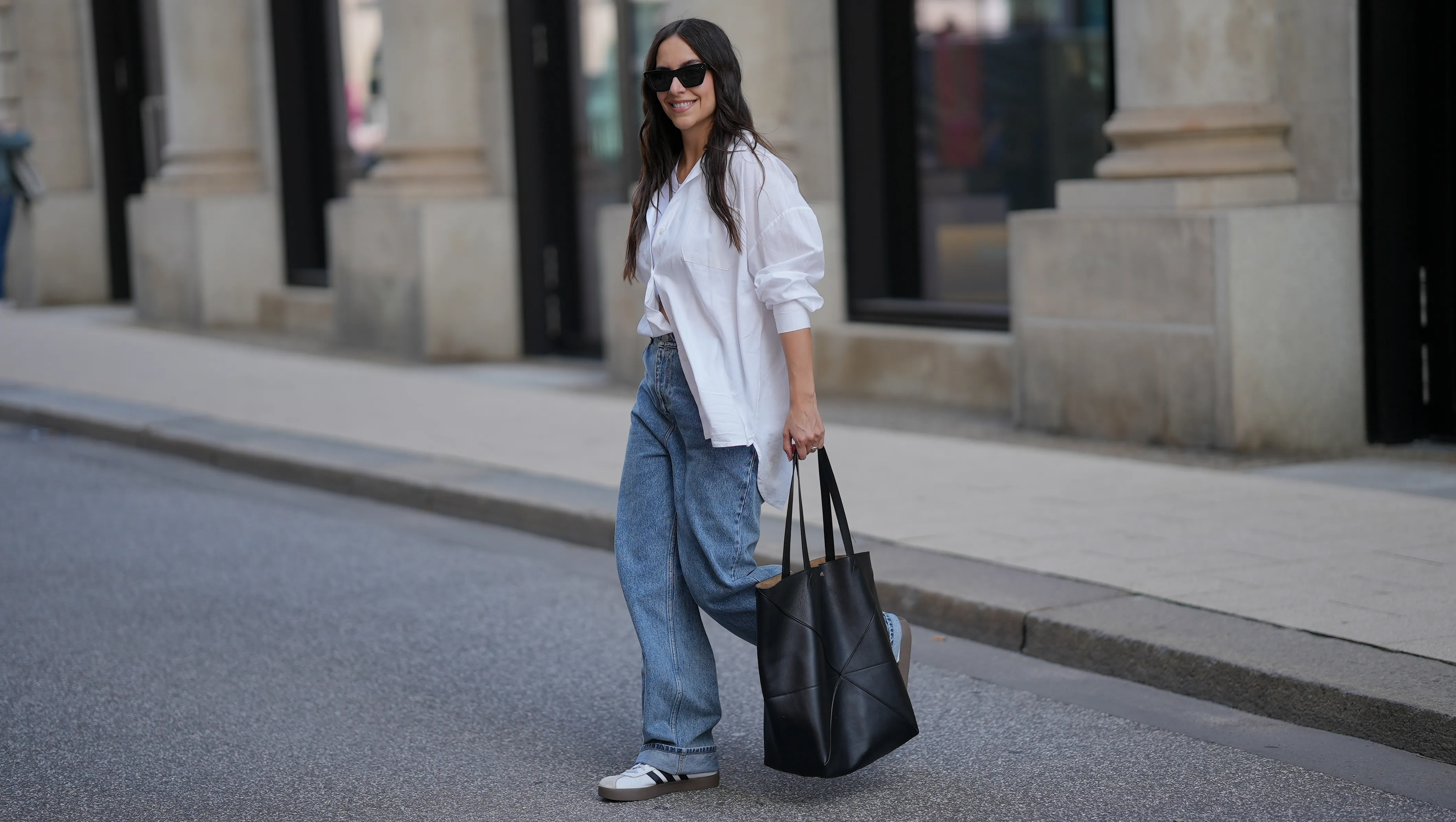 HAMBURG, GERMANY - SEPTEMBER 19: Jessica Schöne is seen wearing an oversized crisp white button-up shirt with a relaxed fit and rolled up sleeves, worn partially tucked into the front of her jeans; a white crew-neck T-shirt layered underneath; light blue straight-leg jeans with a loose, slightly slouchy silhouette; white low-top Adidas VL Court 3.0 sneakers with contrasting brown soles and black side stripes from Adidas; a large folded black leather Puzzle Tote shopper bag from Loewe; stacked gold and silver rings on her fingers; black acetate cat eye sunglasses; her long dark hair is worn down in soft natural waves on September 19, 2025 in Hamburg, Germany. (Photo by Moritz Scholz/Getty Images)