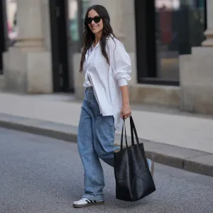 HAMBURG, GERMANY - SEPTEMBER 19: Jessica Schöne is seen wearing an oversized crisp white button-up shirt with a relaxed fit and rolled up sleeves, worn partially tucked into the front of her jeans; a white crew-neck T-shirt layered underneath; light blue straight-leg jeans with a loose, slightly slouchy silhouette; white low-top Adidas VL Court 3.0 sneakers with contrasting brown soles and black side stripes from Adidas; a large folded black leather Puzzle Tote shopper bag from Loewe; stacked gold and silver rings on her fingers; black acetate cat eye sunglasses; her long dark hair is worn down in soft natural waves on September 19, 2025 in Hamburg, Germany. (Photo by Moritz Scholz/Getty Images)