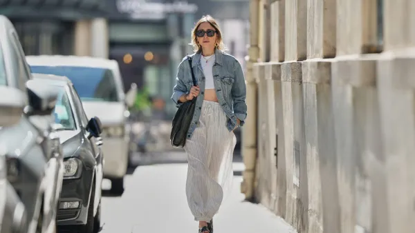 PARIS, FRANCE - SEPTEMBER 06: Emy Venturini wears straight light brown hair with a middle part, black vintage sunglasses, gold hoop earrings, layered necklaces, multiple bracelets, a large black vintage leather shoulder bag, a light blue denim jacket by Levi’s, a white cropped top, wide white striped drawstring pants by Zara Studio, and black leather cross-strap sandals by Prada, during a street style fashion photo session, on September 06, 2025 in Paris, France. (Photo by Edward Berthelot/Getty Images)