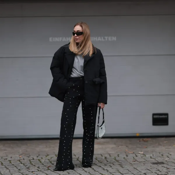 BERLIN, GERMANY - NOVEMBER 15: Sonia Lyson is seen wearing black rectangular sunglasses featuring wide temples with triangular logo embellishments from Prada; silver diamond-studded hoop earrings; a padded black jacket with notch lapels from Marina Hoermanseder x About You; underneath a grey t-shirt from Sézane; wide-legged straight black jeans with rhinestones pattern also from Marina Hoermanseder x About You; a crystal-embellished black leather “Cleo“ bag from Prada; and pointed black leather heels from Jimmy Choo on November 15, 2024 in Berlin, Germany. (Photo by Jeremy Moeller/Getty Images)