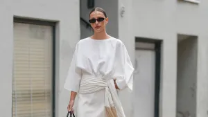 COPENHAGEN, DENMARK - AUGUST 04: A guest wears a white blouse with three-quarter length sleeves and a round neckline. The outfit includes a white skirt with a draped detail and fringe accents. A black shiny leather Birkin handbag from Hermes with a structured shape is held. Black sunglasses with a rectangular frame are worn. Black patent leather heels complete the ensemble. Hair is styled in a sleek, pulled-back manner, outside Freya Dalsjo, during Copenhagen Fashion Week, on August 04, 2025 in Copenhagen, Denmark (Photo by Edward Berthelot/Getty Images)