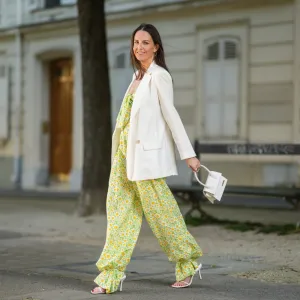 PARIS, FRANCE - APRIL 22: Alba Garavito Torre wears gold earrings, a green with white daisy pattern Mirae jumpsuit with off shoulder knotted neck and puffy ankles, a white long blazer jacket, a gold and rhinestones bracelet, gold rings, a gold pink APM Monaco bracelet, a white shiny leather Le Chiquito medium Jacquemus handbag, white matte leather strappy Bottega Veneta sandals heels pumps shoes, on April 22, 2021 in Paris, France. (Photo by Edward Berthelot/Getty Images)