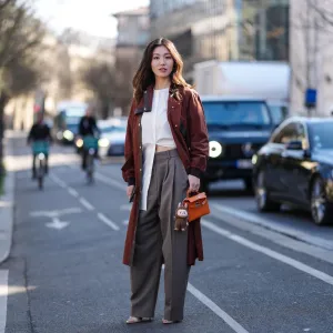 PARIS, FRANCE - MARCH 08: Cristine Sun wears burgundy bordeaux trench coat, white shirt, light gray high waisted trouser pants, shiny dark orange Hermès Kelly leather bag, dark brown Labubu charm, outside Hermès, during the Paris Fashion week Women's Fall/Winter 2025-2026 on March 8, 2025 in Paris, France. (Photo by Edward Berthelot/Getty Images)