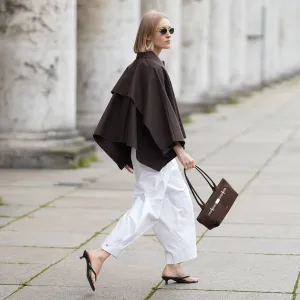 MUNICH, GERMANY - SEPTEMBER 2: Marlies Pia Pfeifhofer is seen wearing a voluminous dark brown cropped trench coat cape with wide draped sleeves from COS; white barrel trousers with ankle length and wide leg silhouette from COS; a pair of black flip-flop heeled sandals with square toes from H&M; a dark brown suede The New York shoulder bag with top handles, triangular fold design and golden hardware from DeMellier; round sunglasses with slim golden frames and dark-shaded lenses from Persol; her blonde bob hair is styled in a sleek, chin-length cut with a center parting on September 2, 2025 in Munich, Germany. (Photo by Moritz Scholz/Getty Images)