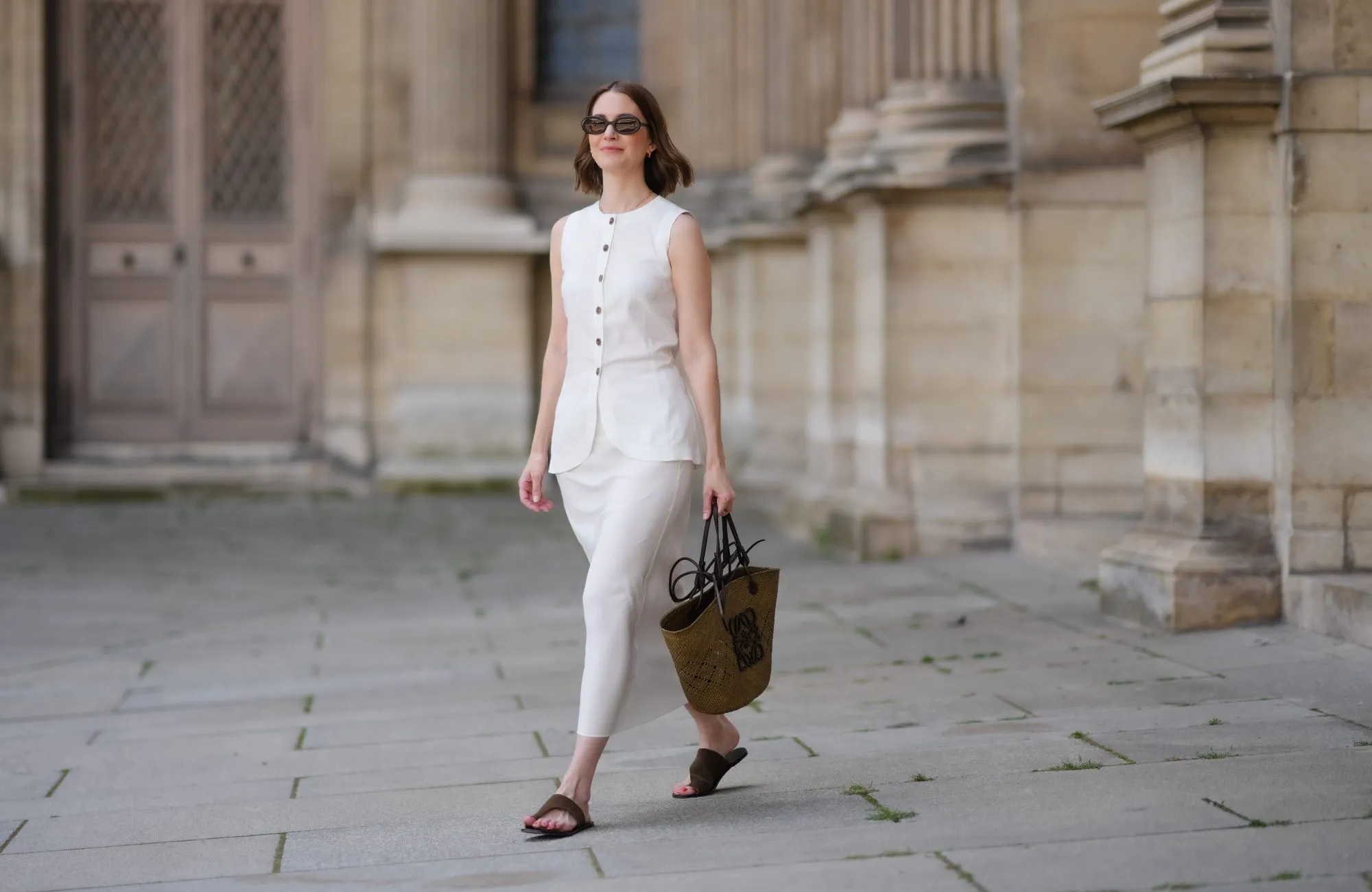 PARIS, FRANCE - MAY 25: Marissa Cox wears a white Arket linen skirt set, a sleeveless long top with buttons, a brown raffia Loewe basket bag, ATP Atelier brown suede sandals / shoes, Jimmy Fairly x Reformation sunglasses, during a street style fashion photo session, on May 25, 2024 in Paris, France. (Photo by Edward Berthelot/Getty Images)