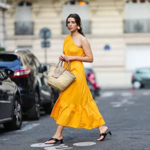 PARIS, FRANCE - AUGUST 12: Ketevan Giorgadze @katie.one wears a one shoulder cut out maxi dress in orange from Mango, oversized golden hoop earrings from Zara, flip flop heeled black sandals shoes from APC Paris, a Le Grand Panier beach straw bag by Jacquemus, on August 12, 2021 in Paris, France. (Photo by Edward Berthelot/Getty Images)