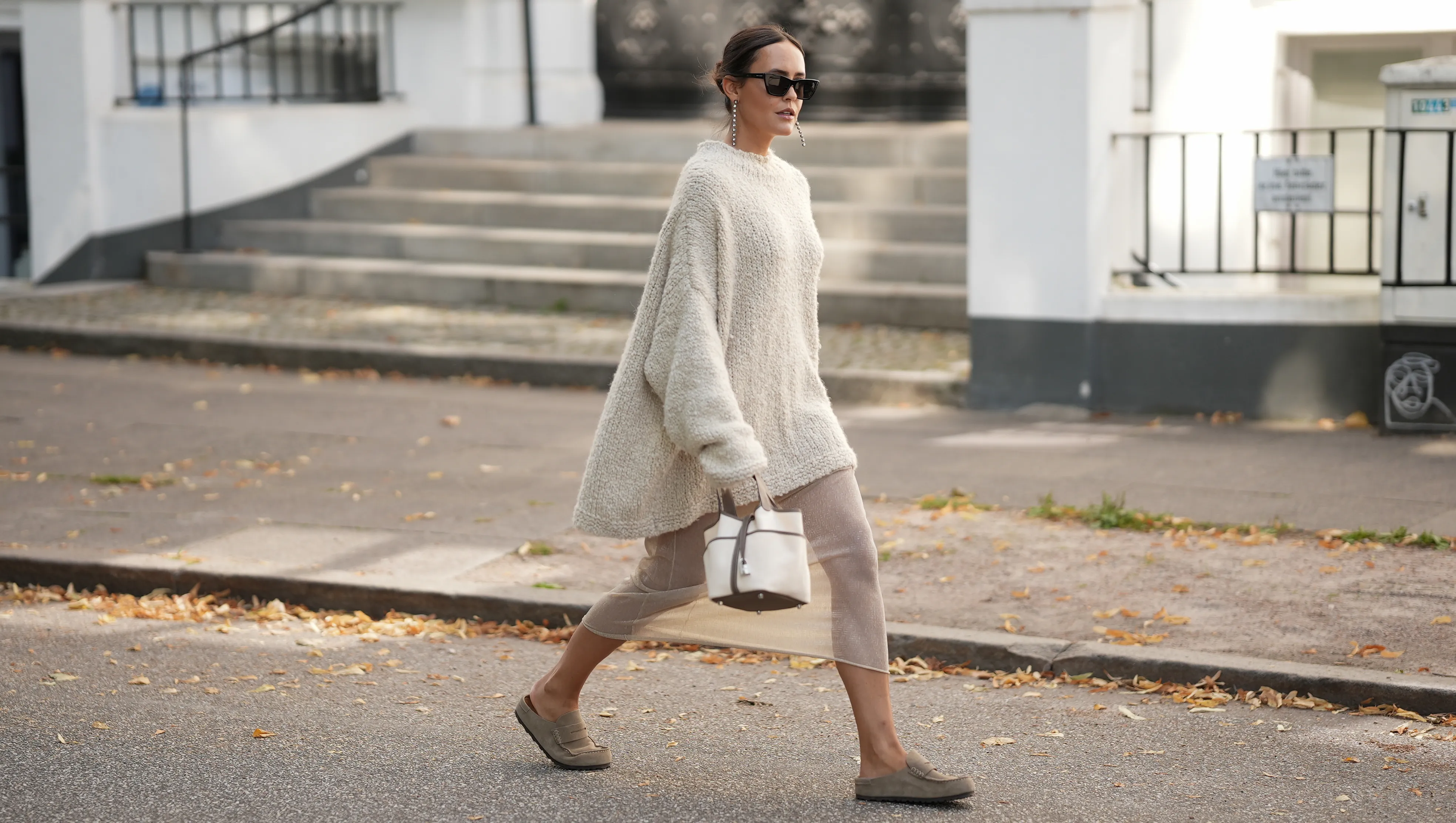 HAMBURG, GERMANY – AUGUST 17: Laura Noltemeyer is seen wearing a loose oversized textured knit sweater in beige from Aylin Koenig; styled underneath with a sheer metallic pleated dress from H&M; paired with taupe suede slip-on loafers from Birkenstock. She is carrying a structured off-white Hermès handbag with dark brown leather trim and handles; accessorized with black rectangular acetate sunglasses from Saint Laurent; hair is parted in the middle and styled in a sleek low ponytail on August 17, 2025 in Hamburg, Germany. (Photo by Moritz Scholz/Getty Images)
