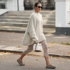HAMBURG, GERMANY – AUGUST 17: Laura Noltemeyer is seen wearing a loose oversized textured knit sweater in beige from Aylin Koenig; styled underneath with a sheer metallic pleated dress from H&M; paired with taupe suede slip-on loafers from Birkenstock. She is carrying a structured off-white Hermès handbag with dark brown leather trim and handles; accessorized with black rectangular acetate sunglasses from Saint Laurent; hair is parted in the middle and styled in a sleek low ponytail on August 17, 2025 in Hamburg, Germany. (Photo by Moritz Scholz/Getty Images)