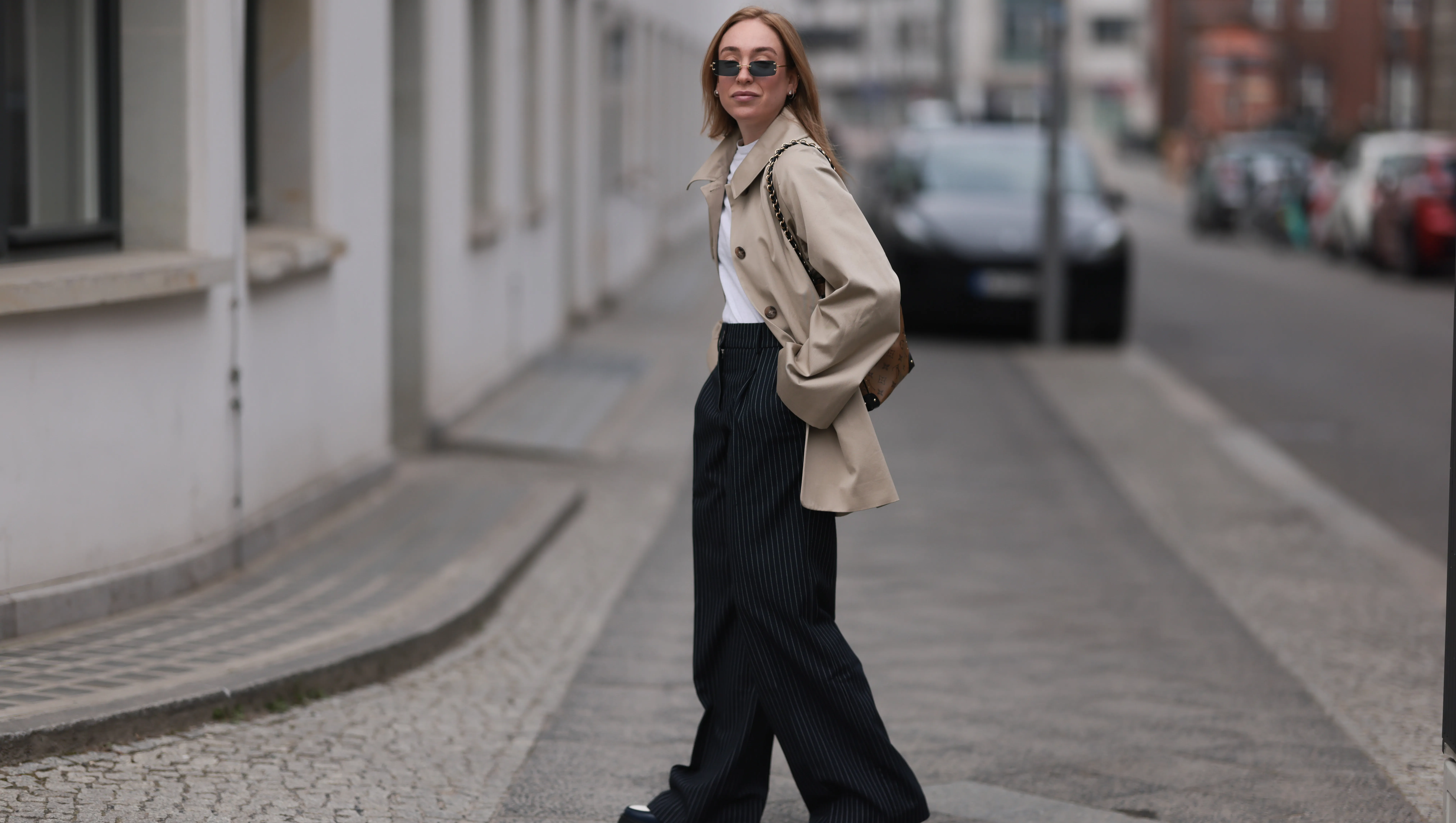 BERLIN, GERMANY - MARCH 24: Sonia Lyson seen wearing Linda Farrow black rectangular sunglasses with dark lenses, adding a modern and edgy touch, Sézane classic white crew-neck cotton t-shirt, Sézane beige oversized trench coat with large statement buttons and a relaxed fit, Sézane high-waisted black pinstriped wide-leg trousers, Louis Vuitton brown logo monogram pattern bucket bag with gold chain straps adds a sophisticated contrast and Sézane black-and-white leather platform loafer shoes with a chunky sole, on March 24, 2025 in Berlin, Germany. (Photo by Jeremy Moeller/Getty Images)