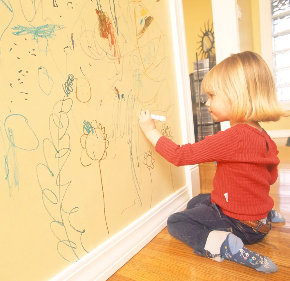 Little girl writing on the wall of her house.