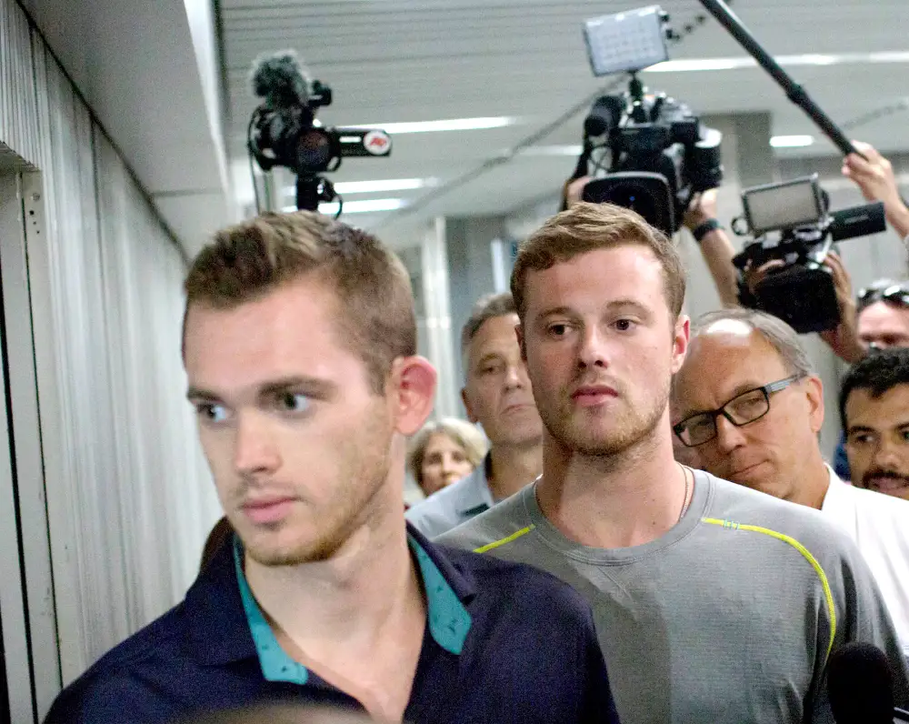 Journalists surround American Olympic swimmers Gunnar Bentz, left, and Jack Conger, center, as they leave the police station at Rio International airport early Thursday Aug. 18, 2016.